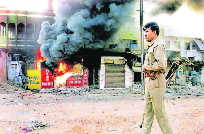 This photo, taken on March 1, 2002, shows a policeman as he walks in front of a row of burning shops in Ahmedabad.